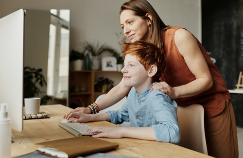A mother and son smile as they look at a desktop computer communicating  with a resident.