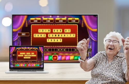 An older adult resident celebrates with joy sitting in front of the UE Live! game displayed on a tablet and tv monitor